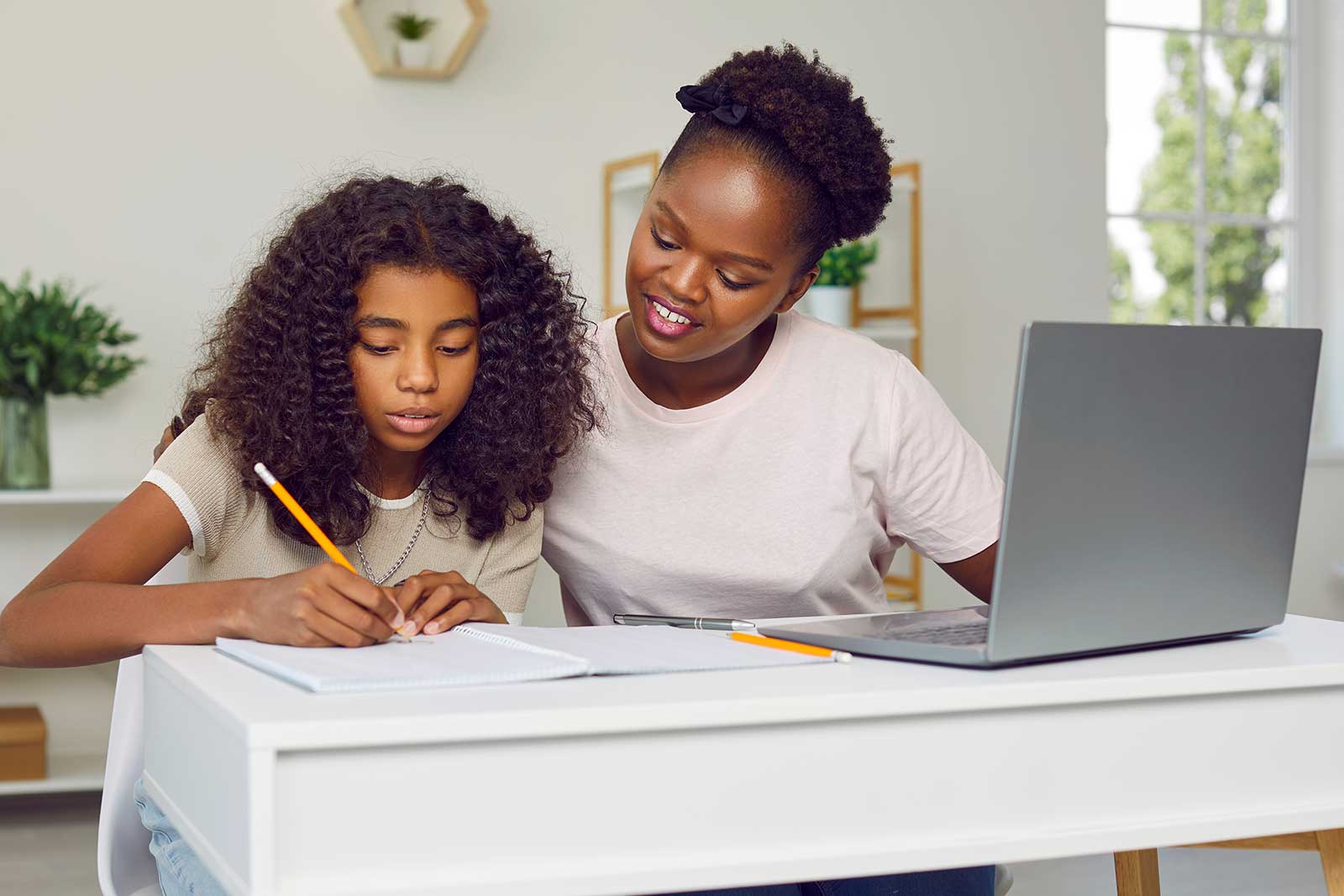 imagen de una madre afroamericana ayudando a su hija a hacer los deberes con un portátil